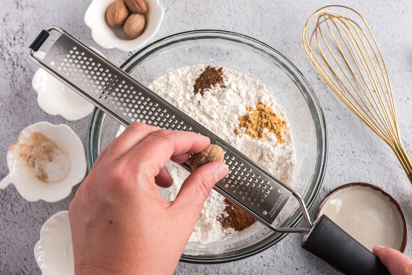 grating nutmeg over flour mixture and spices in a bowl