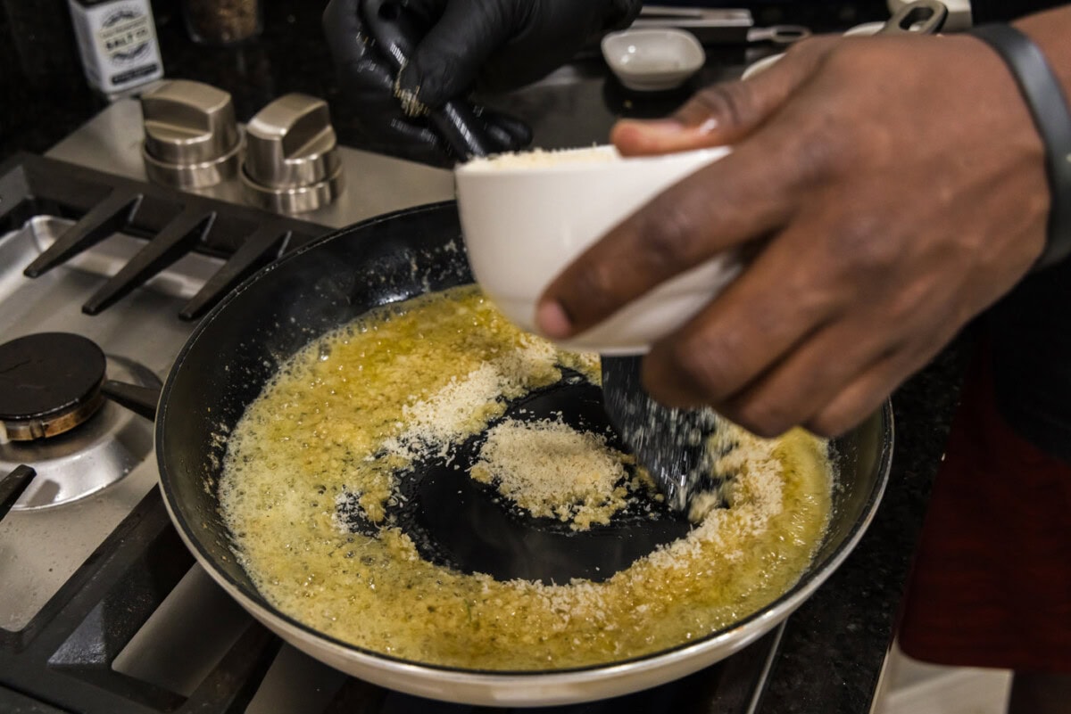 adding parmesan cheese to butter and garlic mixture in a skillet