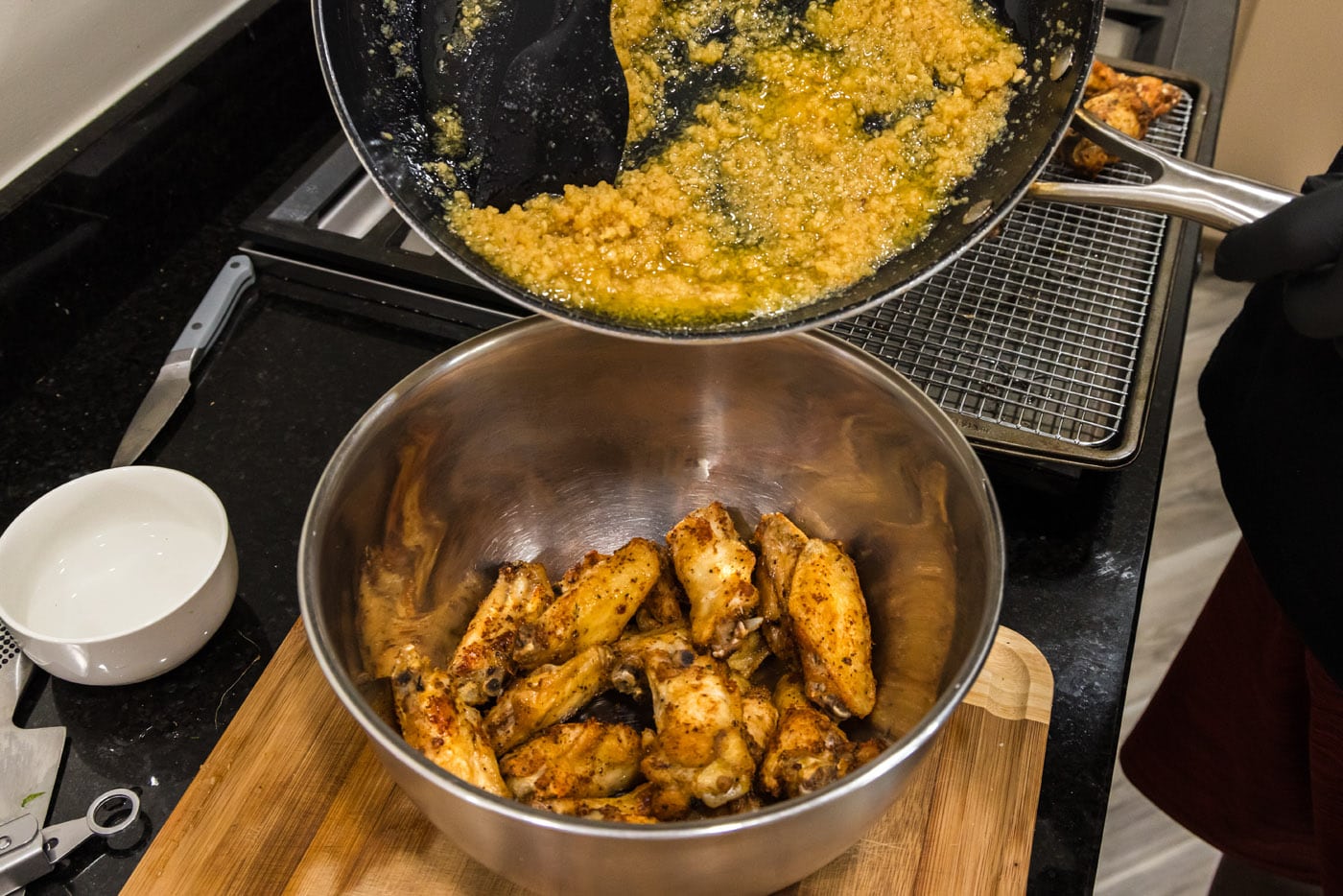 pouring garlic parmesan sauce over chicken wings in a bowl