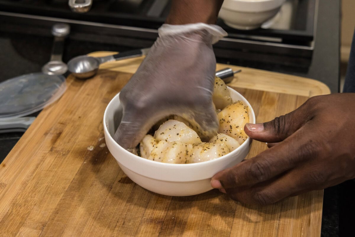 gloved hand mixing scallops with butter mixture
