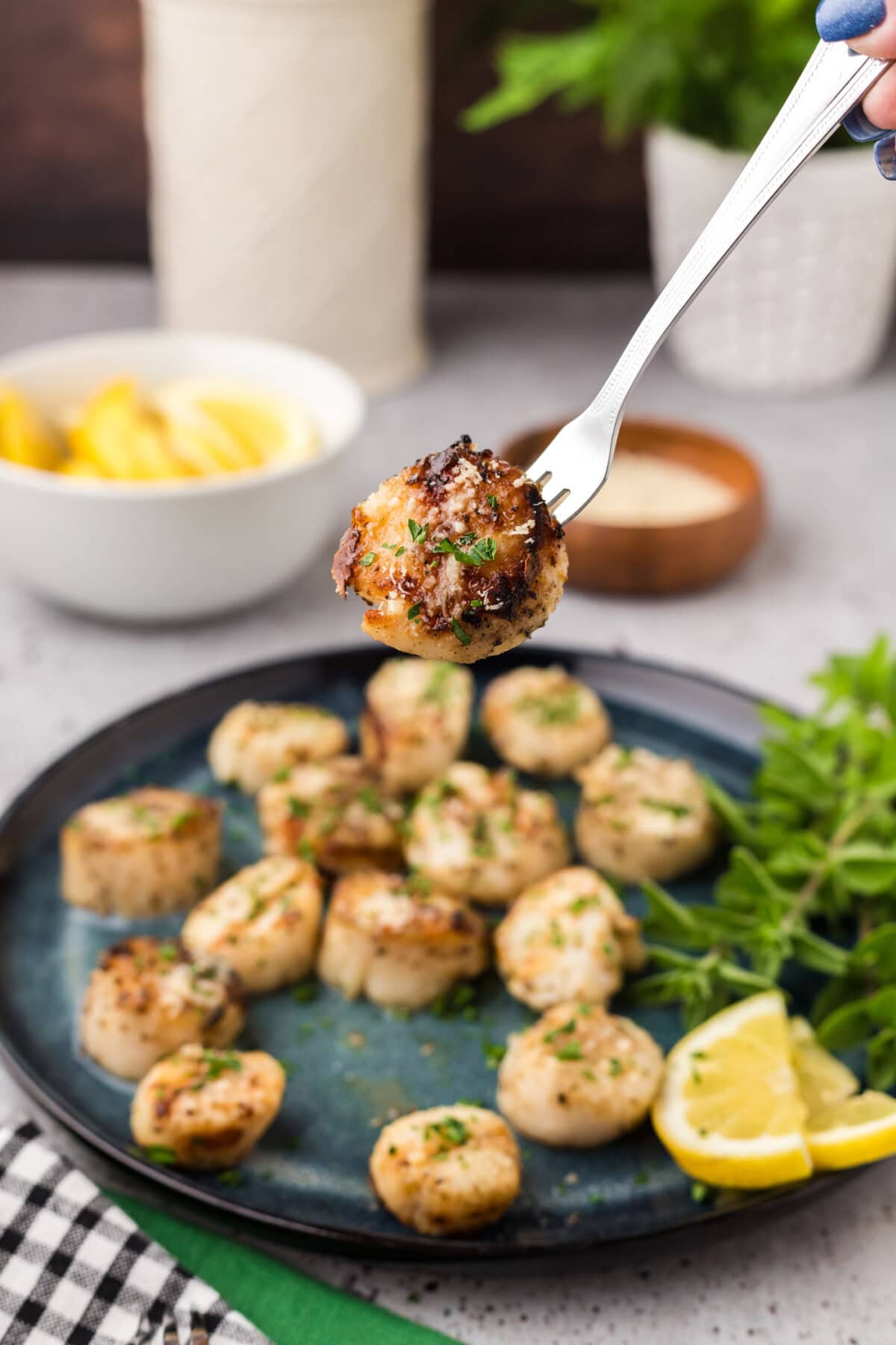 Grilled Scallop on a seafood fork held above a plate of Grilled Scallops