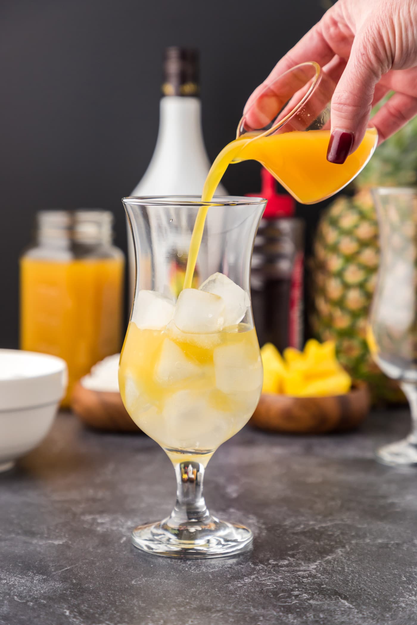 pouring pineapple juice into glass of Malibu rum and ice