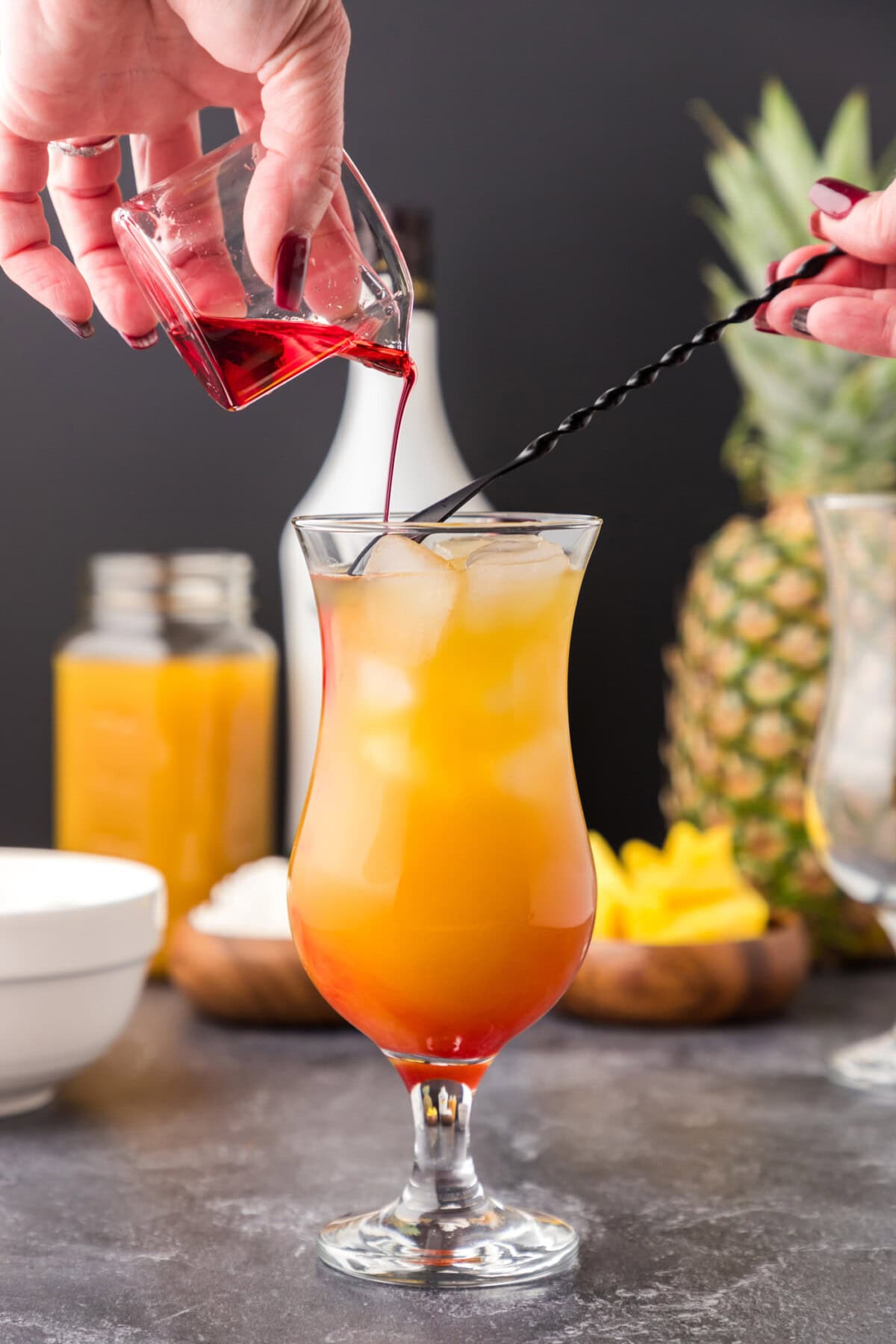carefully pouring grenadine over a cocktail spoon into malibu sunset