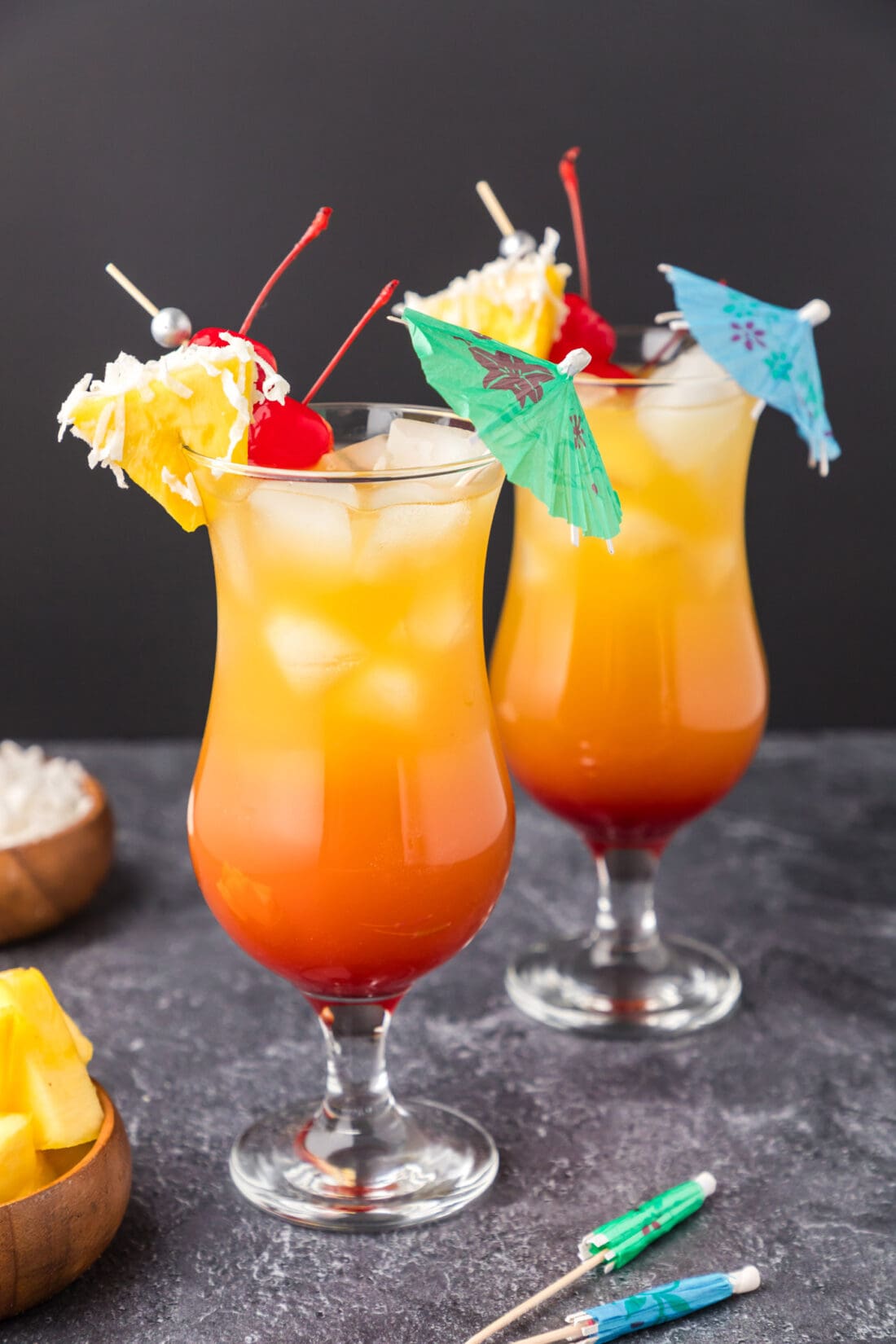 Two Malibu Sunset cocktails garnished with a pineapple wedge, cherry and umbrella
