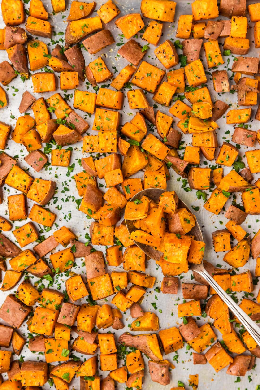 Sheet pan of Roasted Sweet Potatoes with a spoon on the sheet pan