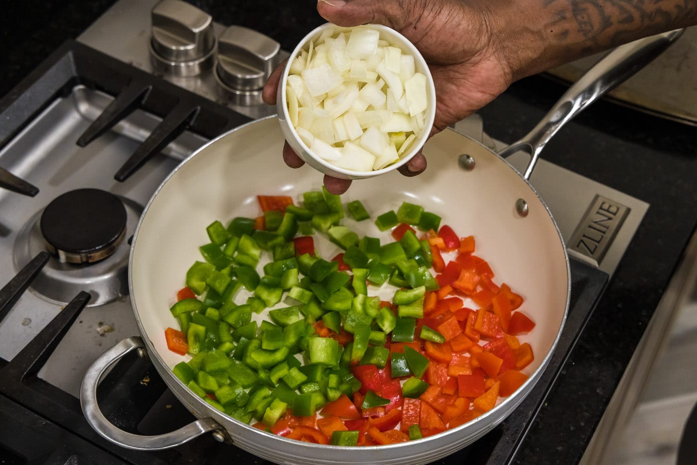 adding onion to bell peppers in a skillet