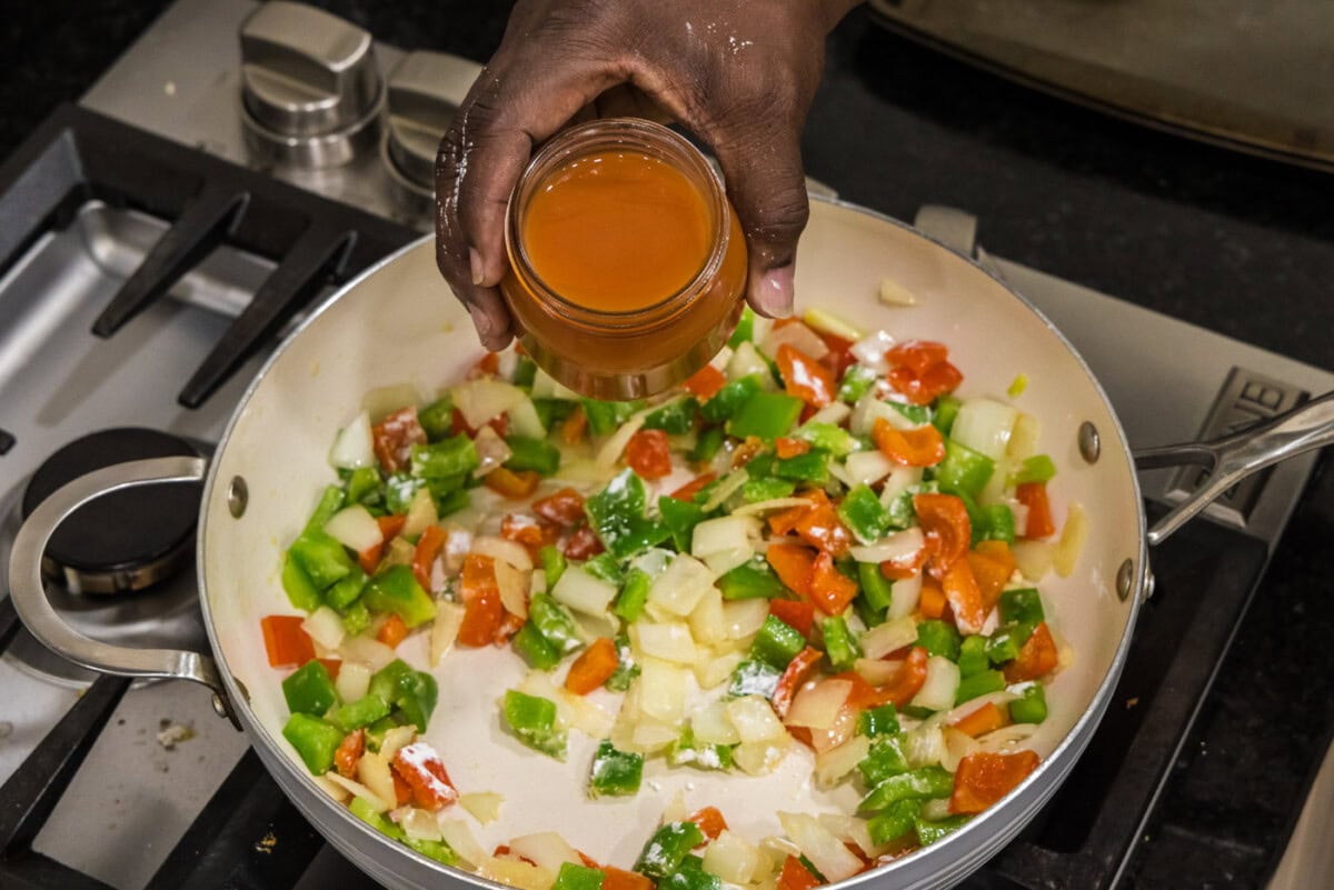 pouring sweet and sour sauce over veggies in a pan