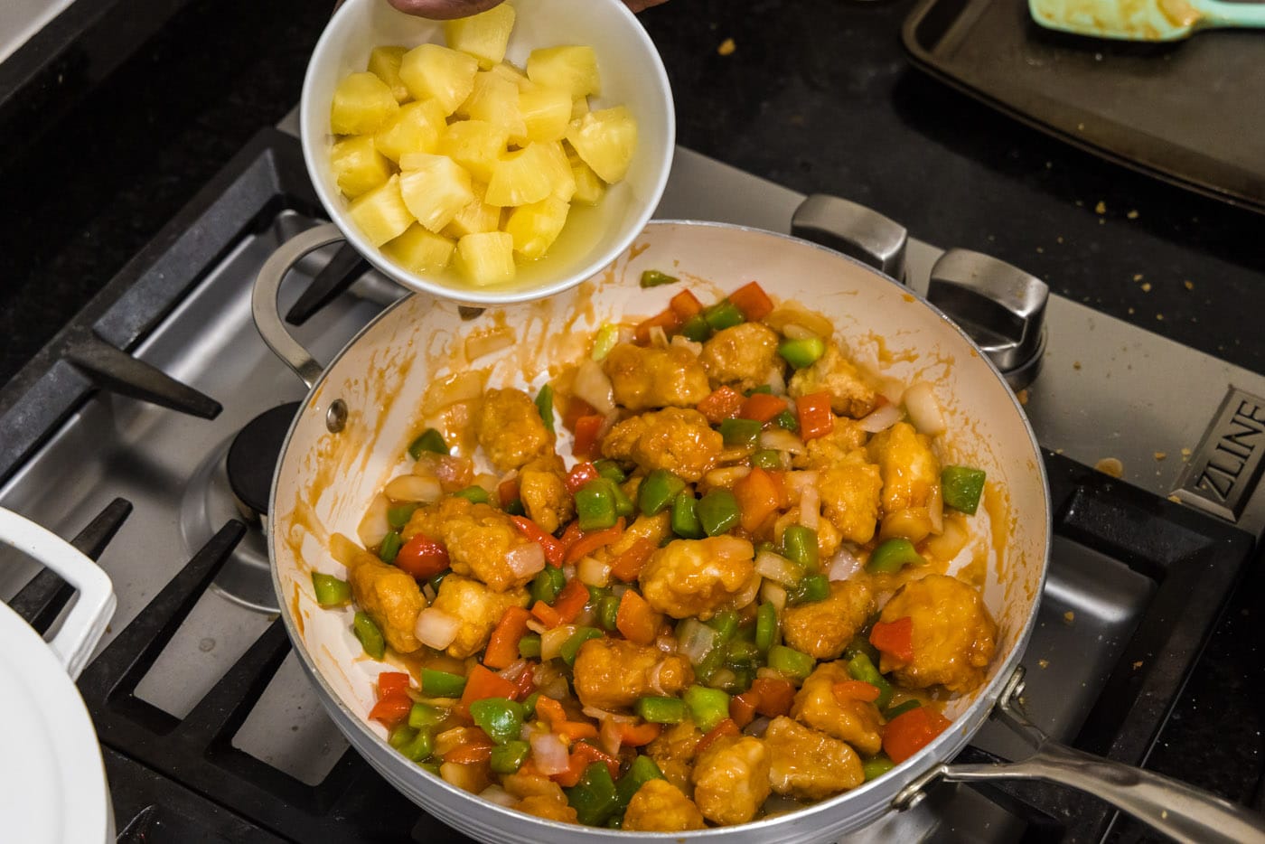 adding pineapple to skillet of sweet and sour chicken