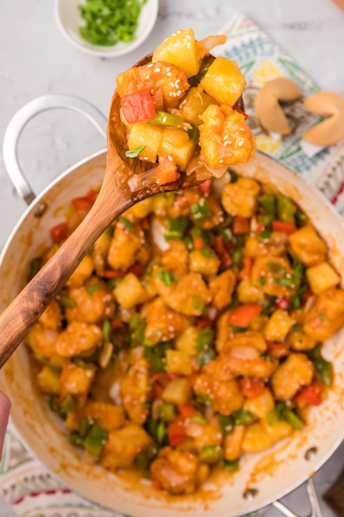 Spoonful of Sweet and Sour Chicken held above a skillet of Sweet and Sour Chicken