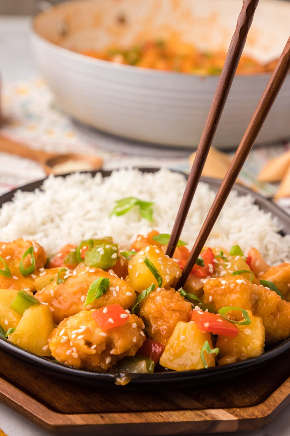Chopsticks grabbing a piece of pineapple from a plate of Sweet and Sour Chicken with rice