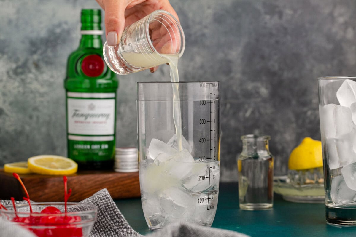 pouring fresh lemon juice over gin in cocktail shaker