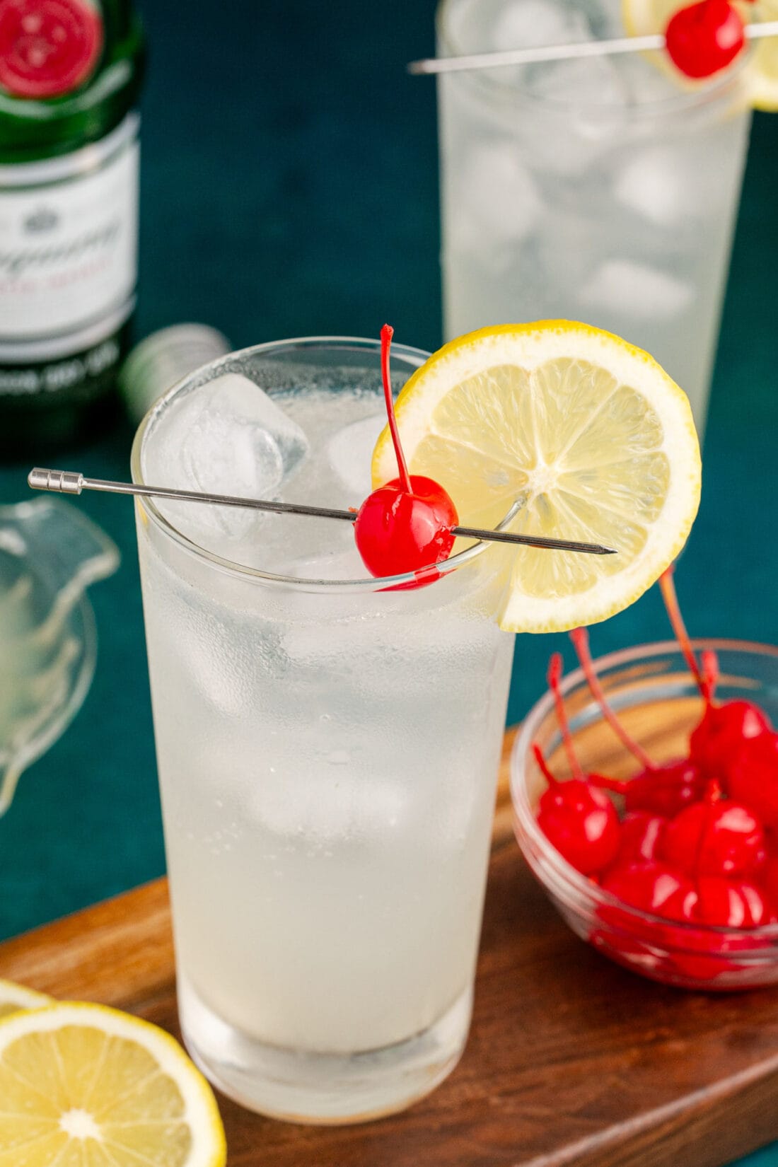 Close up photo of a Tom Collins cocktail garnished with a cherry and lemon wheel
