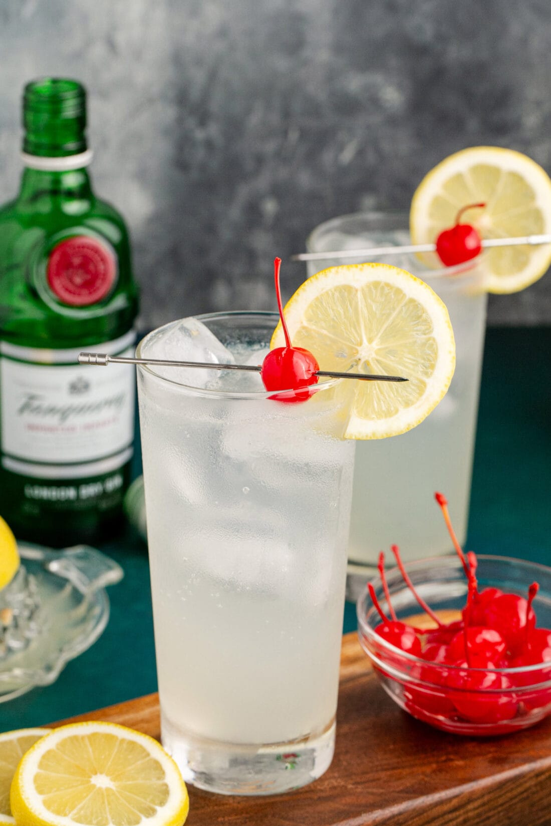 Two Tom Collins cocktails garnished with a lemon wheel and cherry