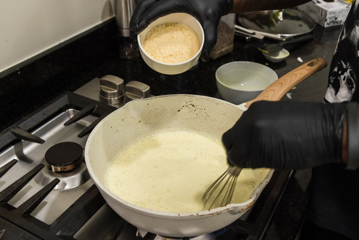 adding parmesan cheese to carbonara sauce in a skillet