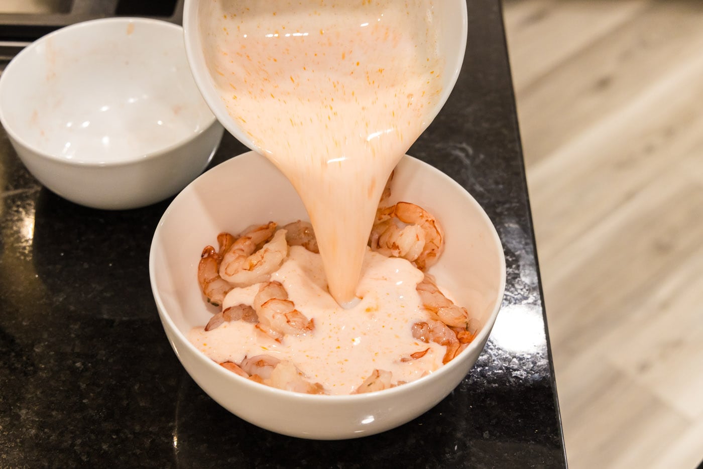 pouring buttermilk hot sauce mixture over shrimp in a bowl