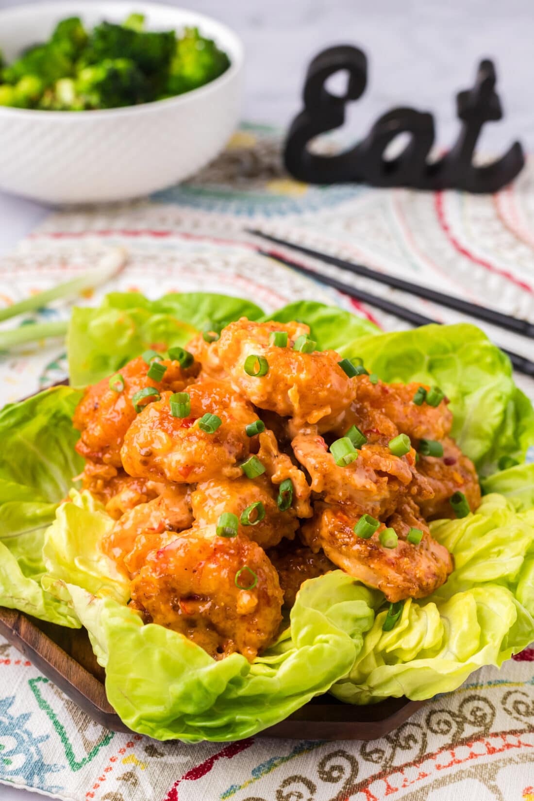 Bang Bang Shrimp on a bed of lettuce with a bowl of broccoli in the background