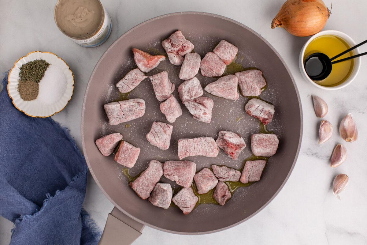 flour coated beef cubes searing in a skillet