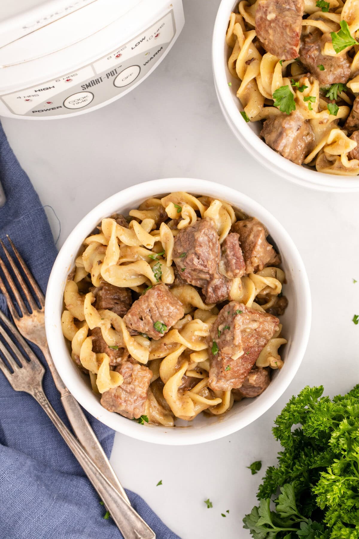 Two bowls of Beef and Noodles with a crockpot in the background
