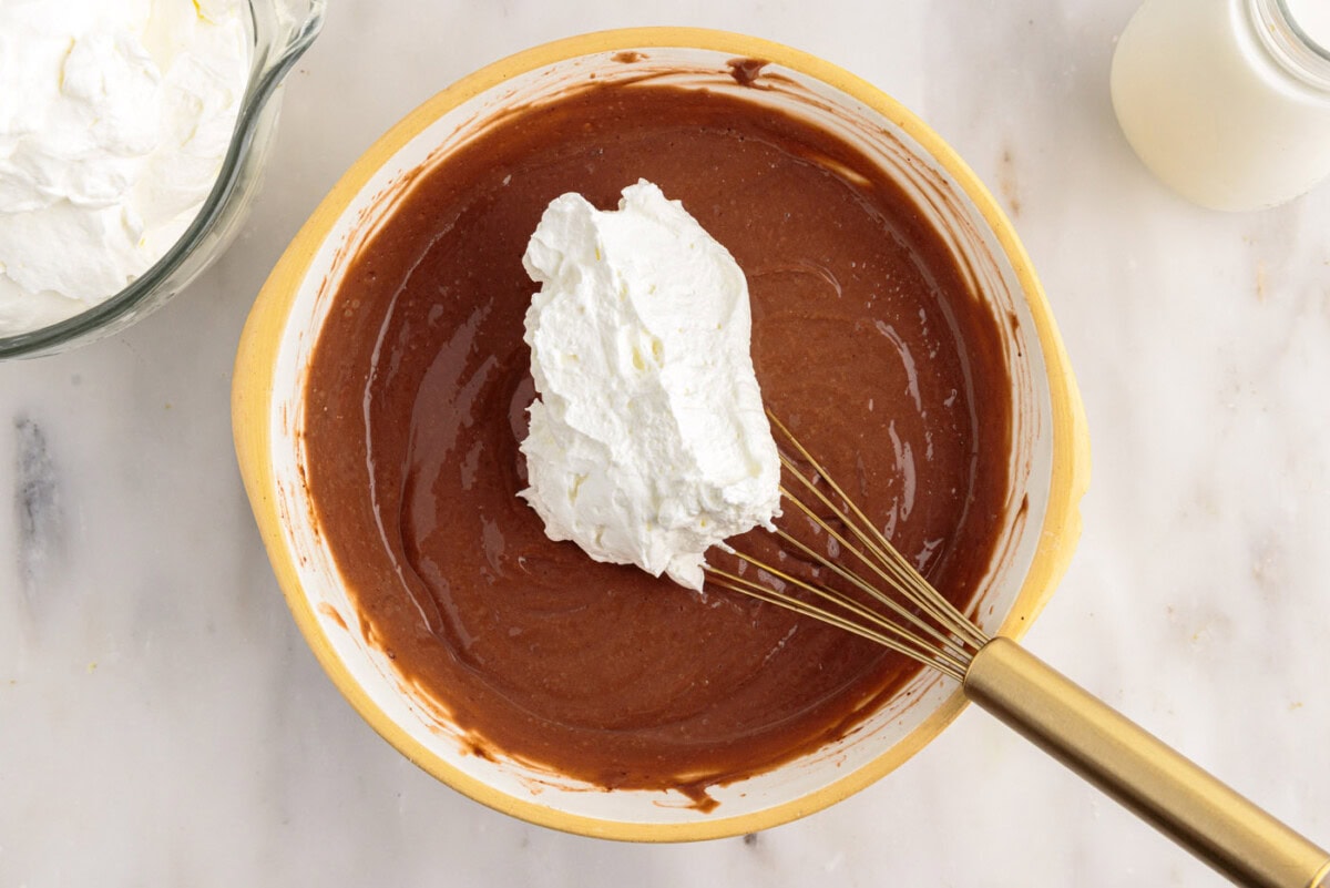 adding whipped cream to chocolate pudding in a bowl
