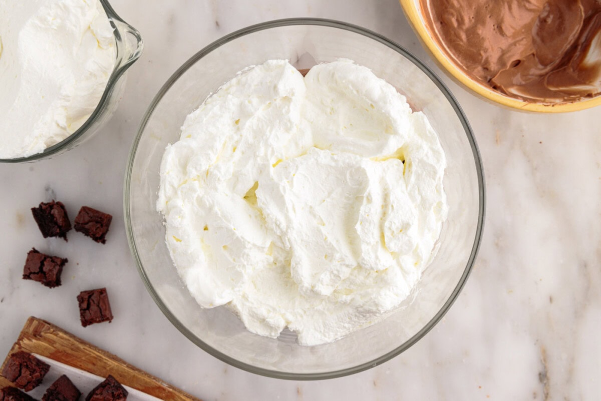 layer of whipped cream on top of chocolate pudding and brownie pieces