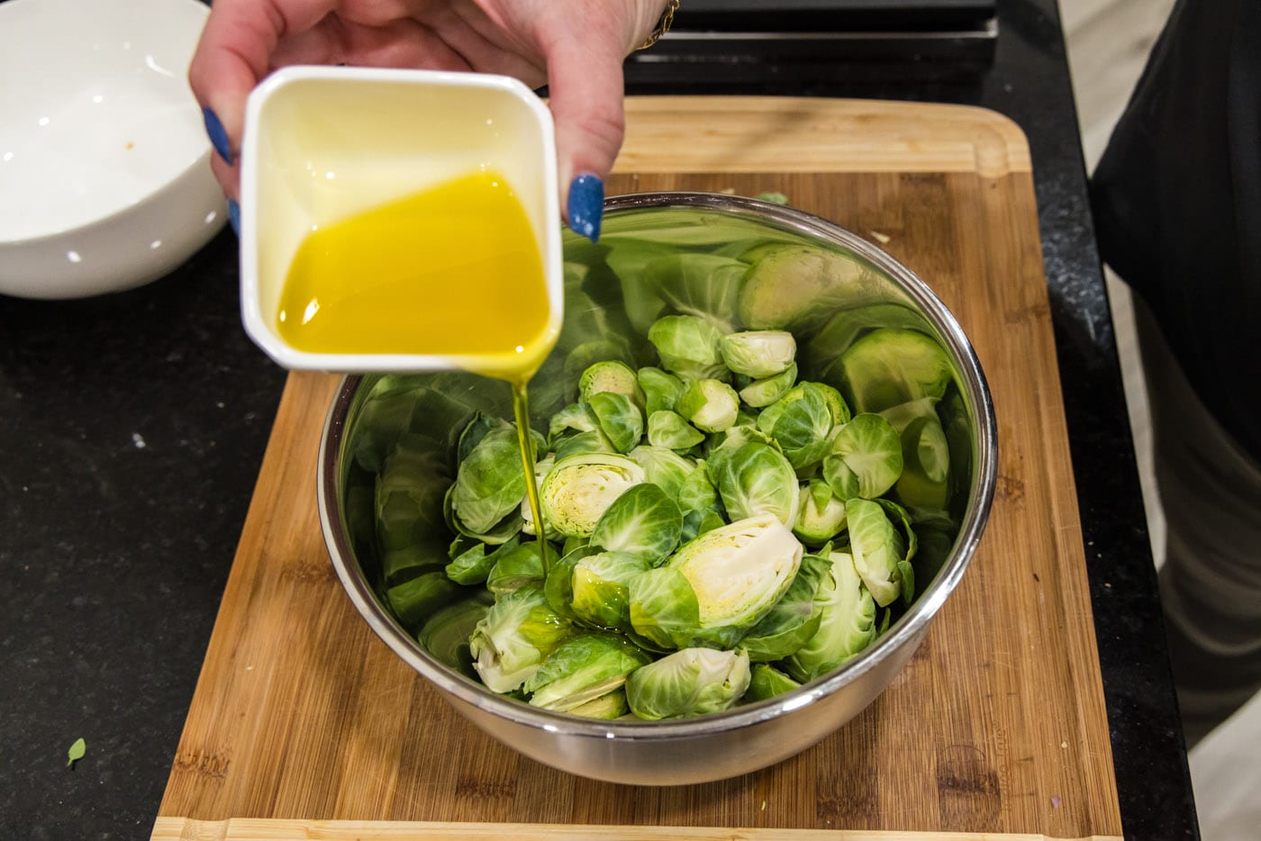 adding olive oil to bowl of brussels sprouts