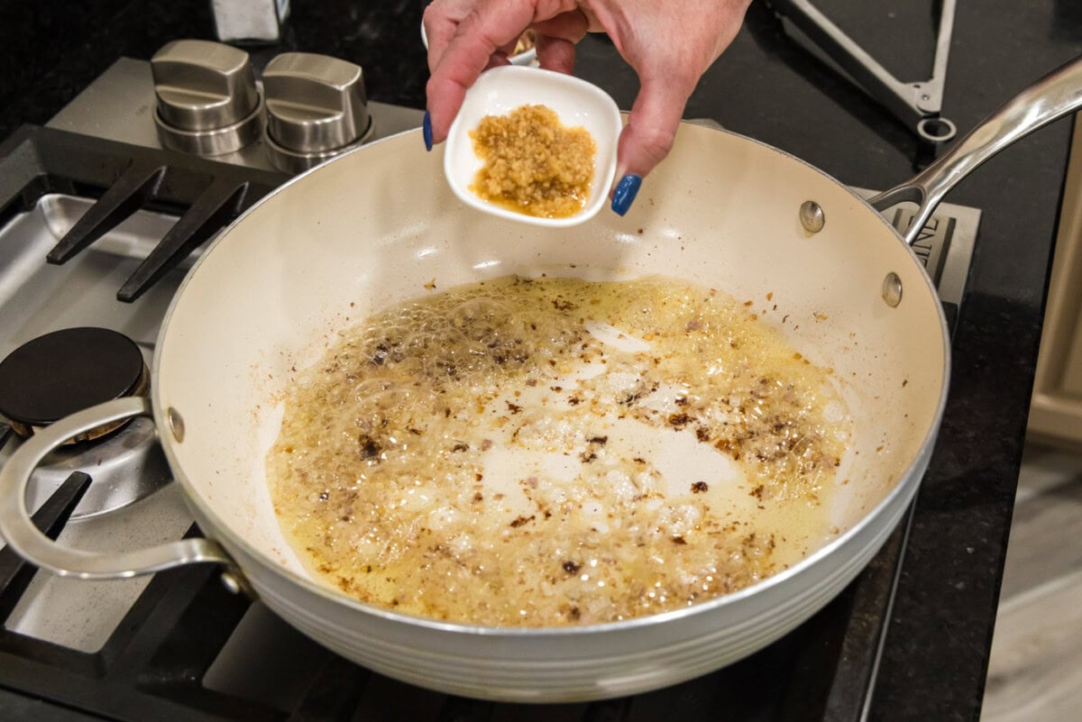 adding garlic to skillet with shallots and oil