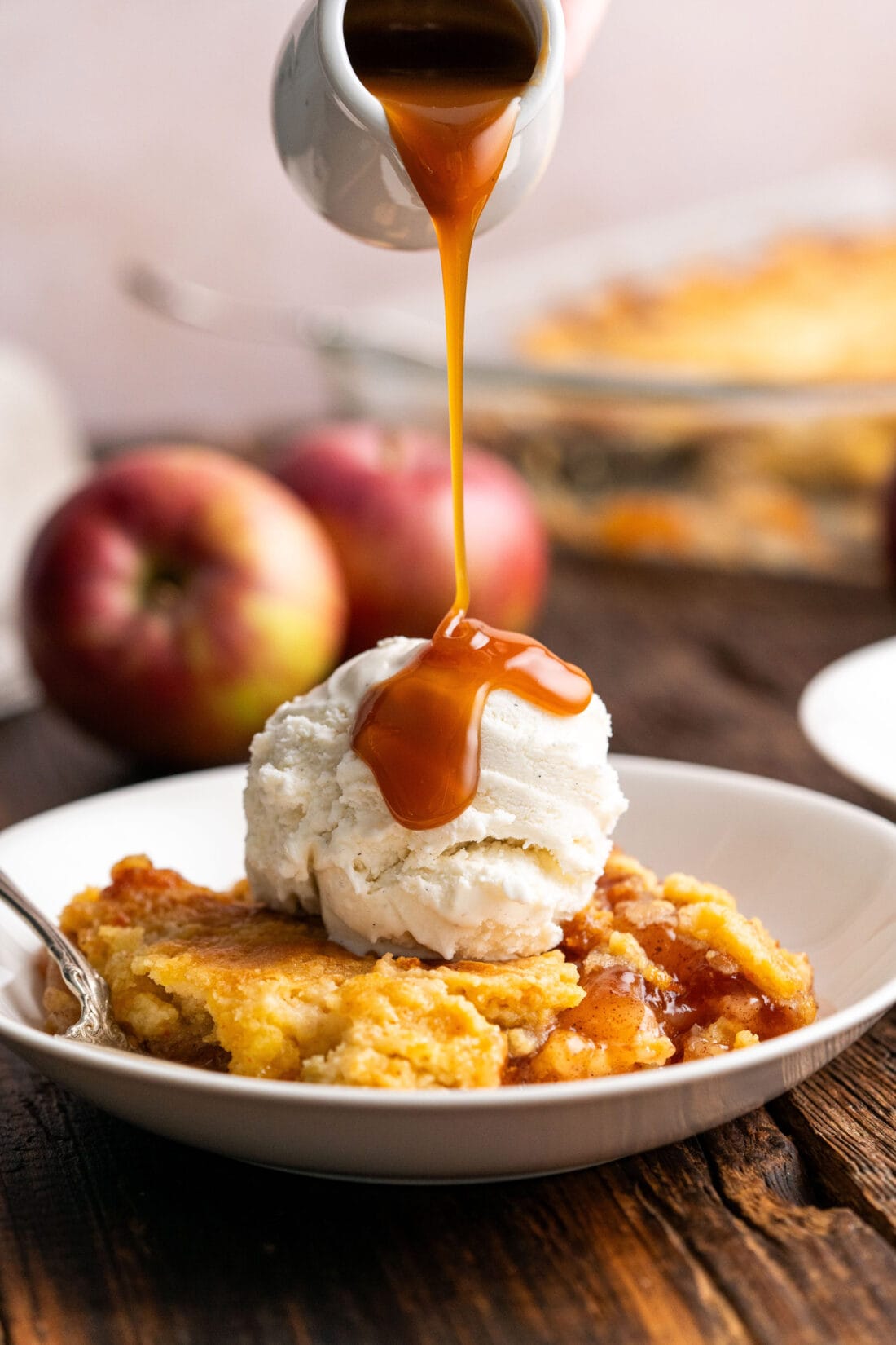 Caramel sauce being drizzled over Caramel Apple Dump Cake topped with ice cream