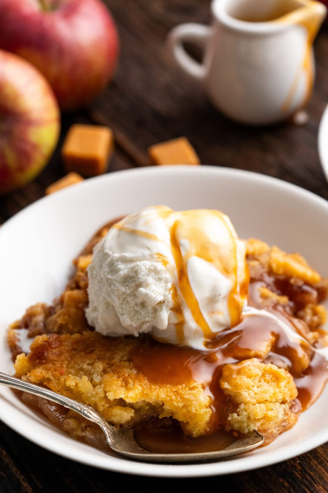 Caramel Apple Dump Cake in a bowl topped with ice cream and caramel sauce
