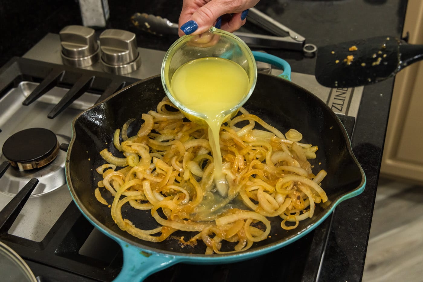 pouring chicken broth into skillet with onions