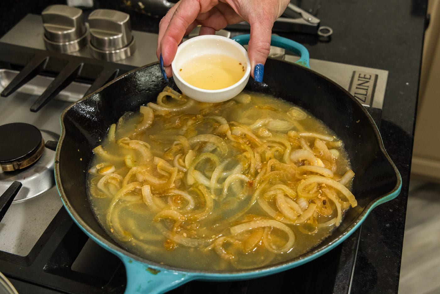 pouring rice vinegar into skillet with onions and chicken broth