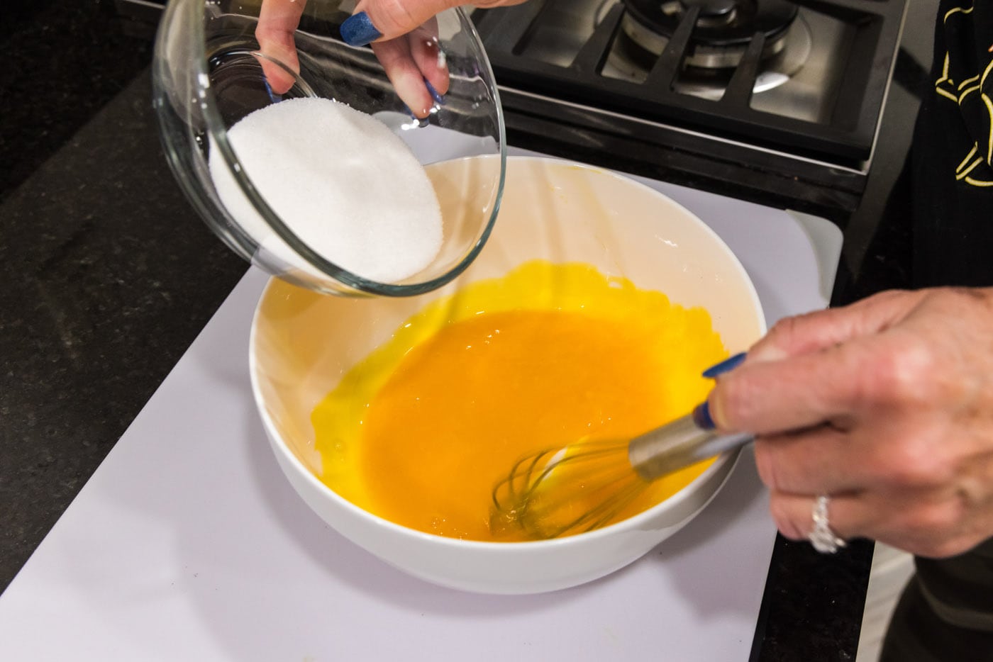 adding sugar to egg yolks in a bowl