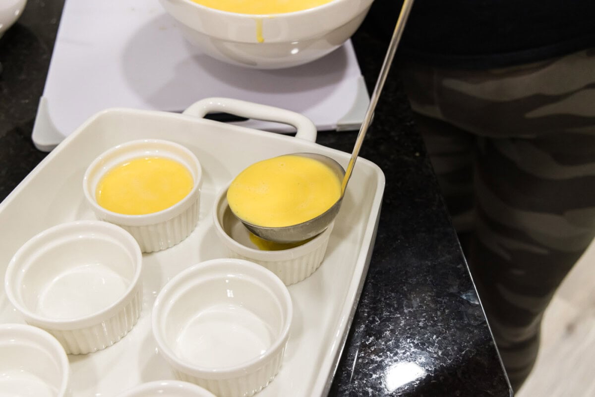 ladle pouring creme brulee filling into a ramekin