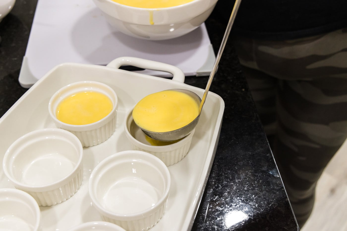 ladle pouring creme brulee filling into a ramekin