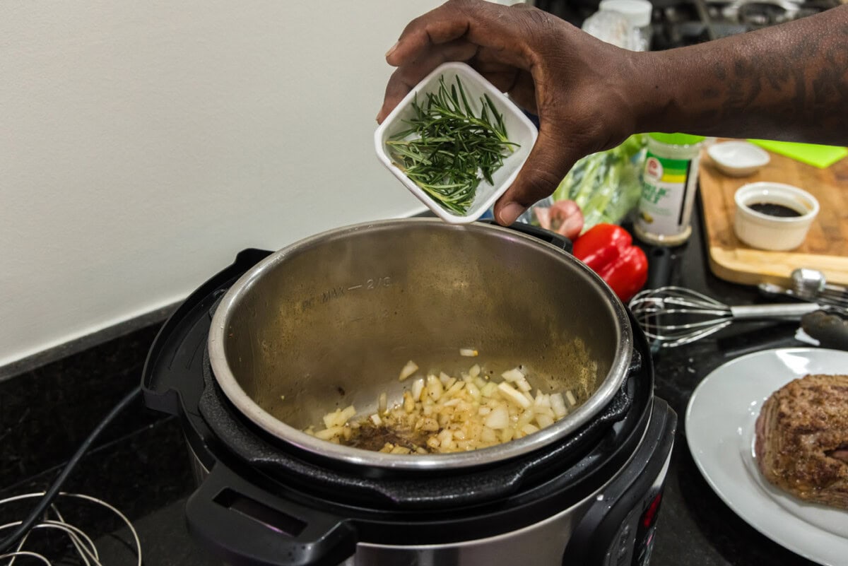 adding rosemary to pot of onions and garlic