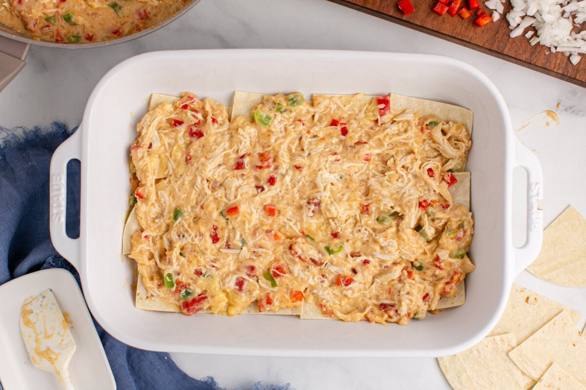 chicken and sauce mixture layered over tortillas in a dish