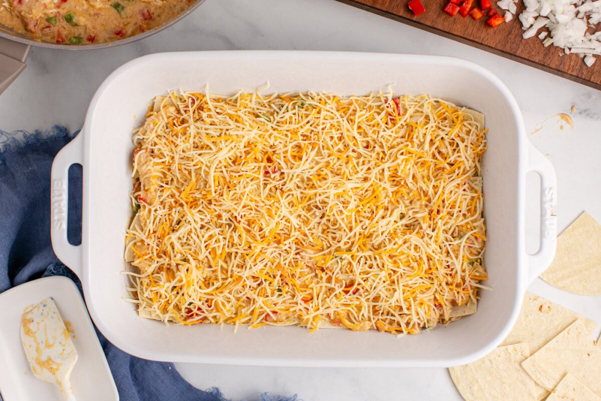 shredded cheese layered over chicken sauce in a baking dish