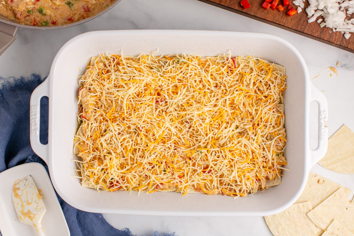 shredded cheese layered over chicken sauce in a baking dish