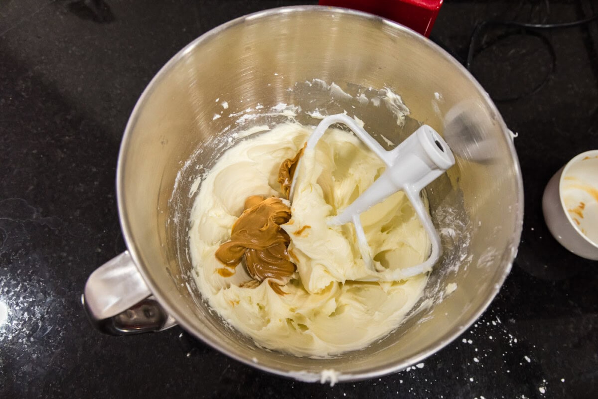 peanut butter added to cream cheese frosting in a bowl of a stand mixer