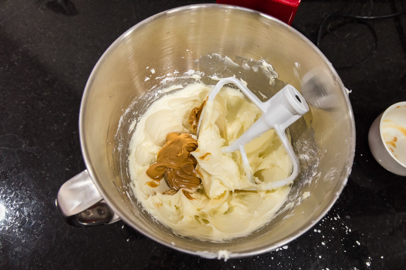 peanut butter added to cream cheese frosting in a bowl of a stand mixer
