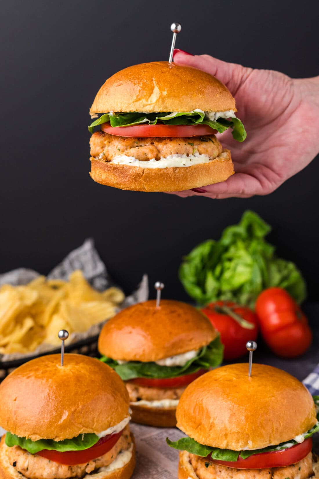 Hand holding up a Salmon Burger above more Salmon Burgers