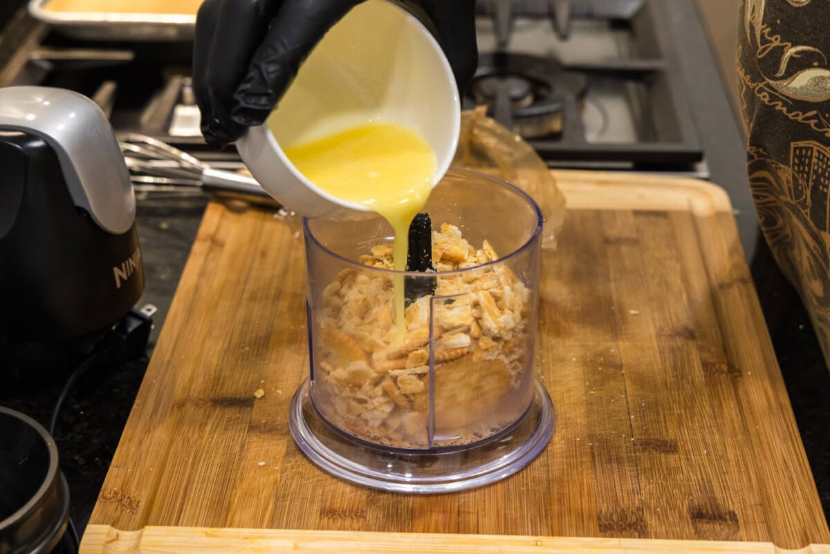 pouring melted butter into crushed ritz crackers in a food processor