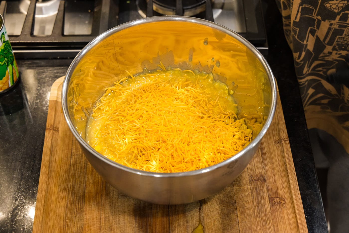shredded cheddar cheese added to canned corn in a mixing bowl