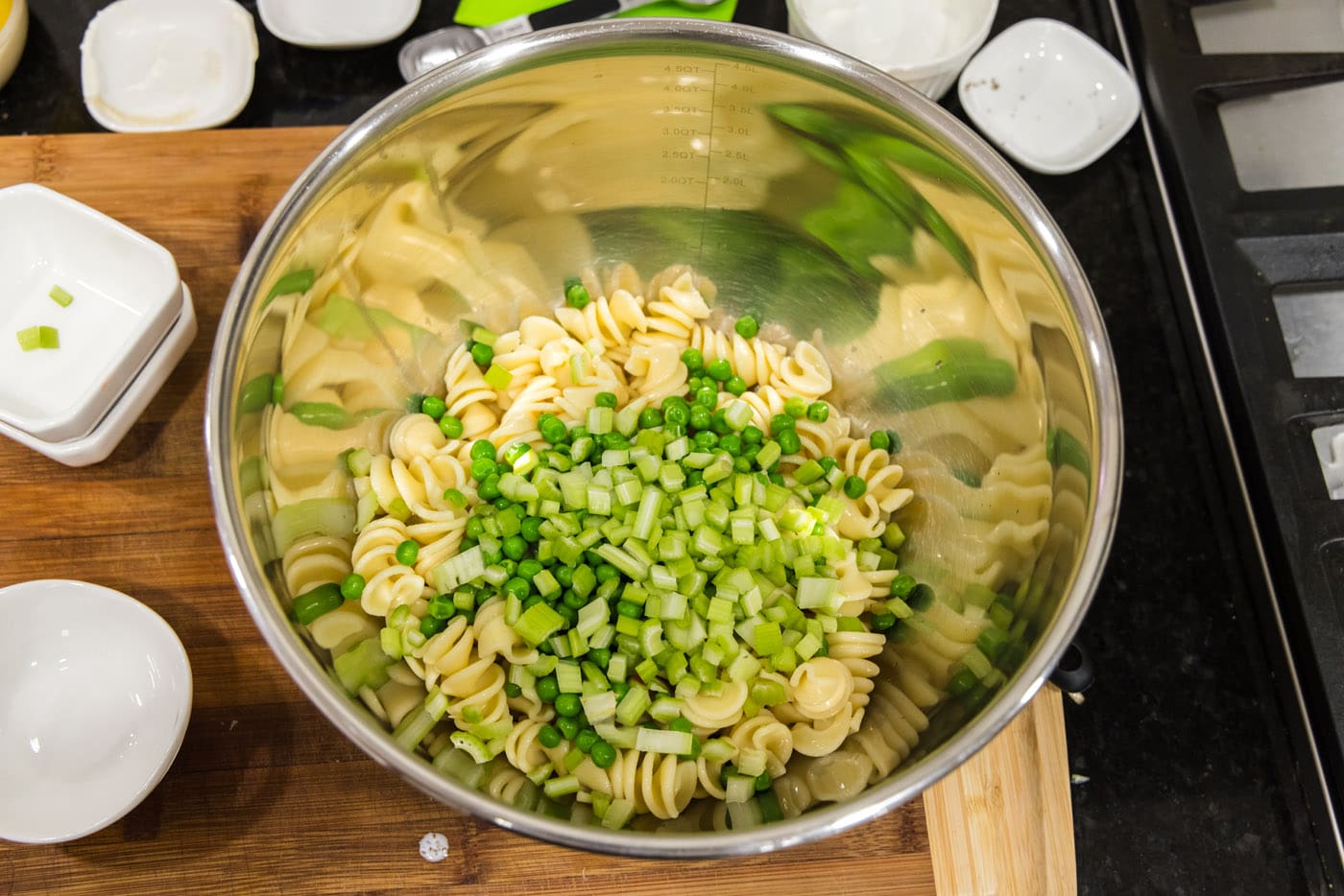 adding chopped celery and peas to bowl with pasta