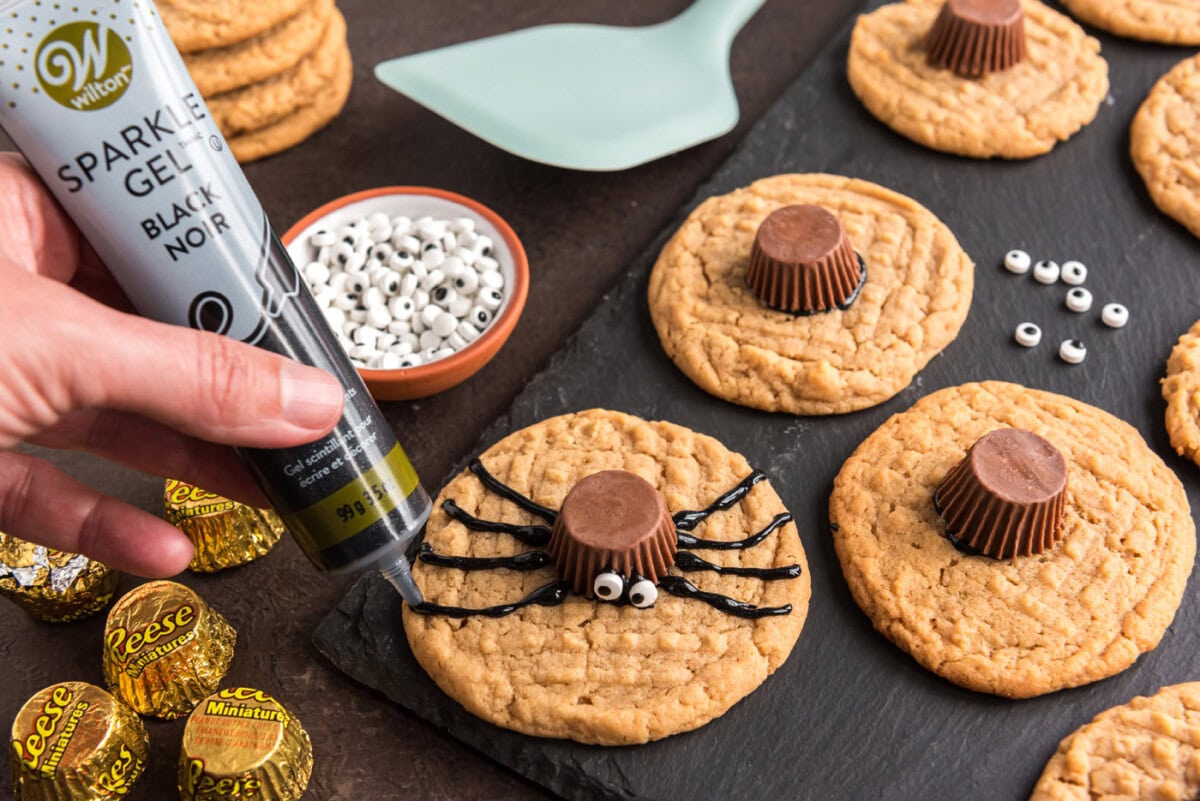 piping black decorator gel onto cookie to make spider legs