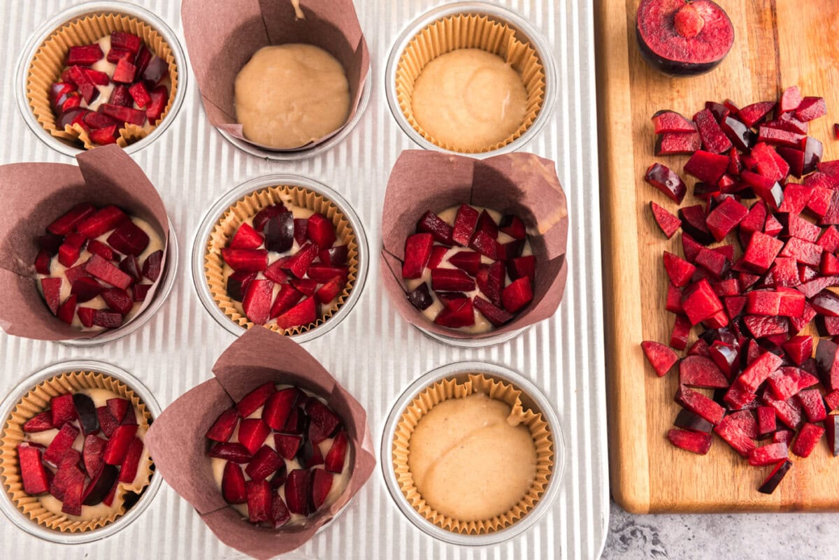 adding diced plums to muffin batter in a muffin pan