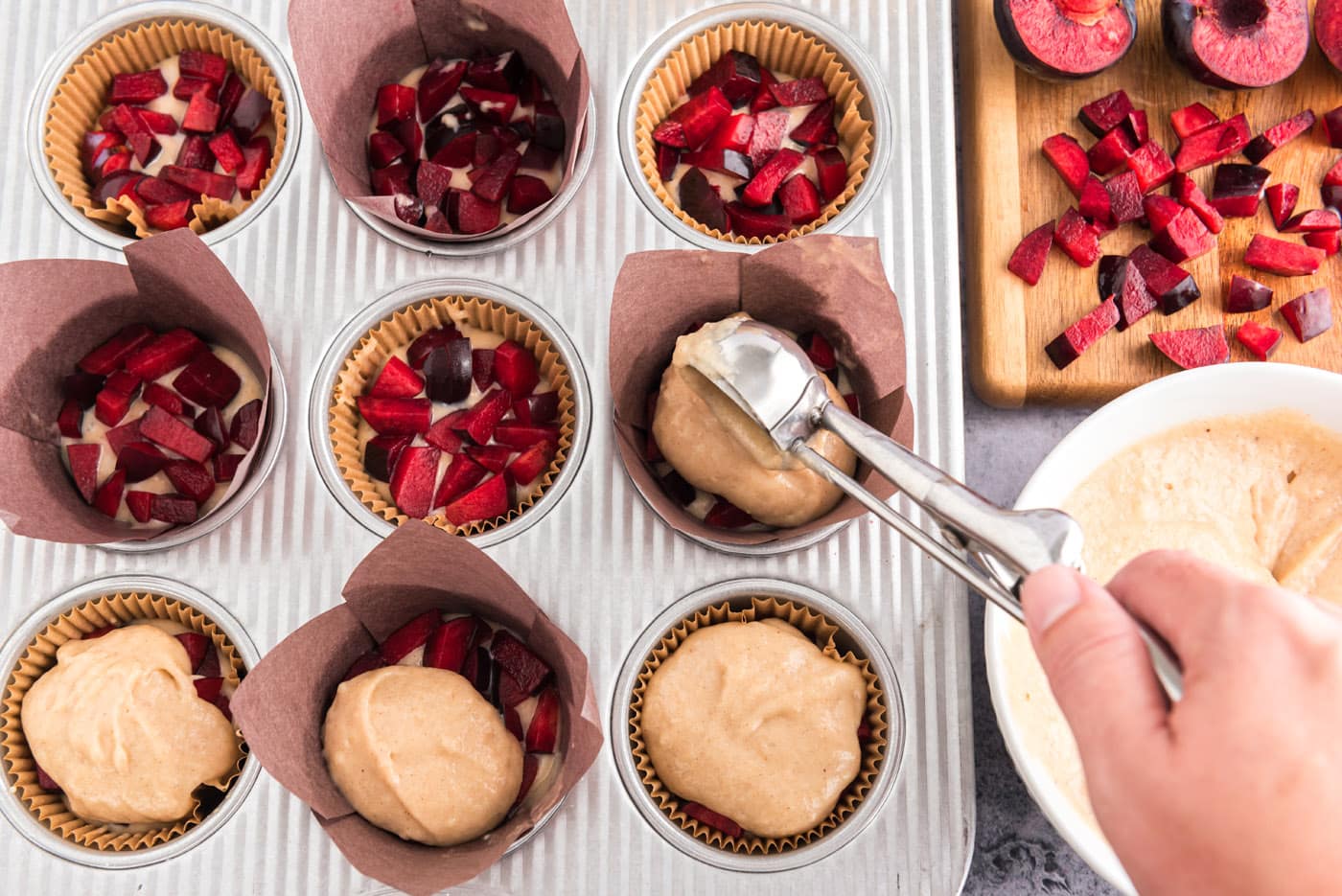 scooping muffin batter over chopped plums