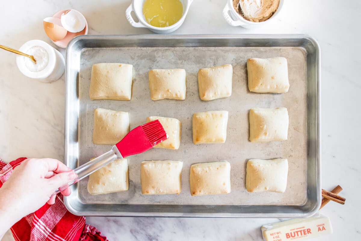 brushing texas roadhouse rolls with melted butter on a baking sheet