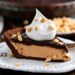 Slice of Chocolate Peanut Butter Pie on a plate topped with cool whip and peanuts