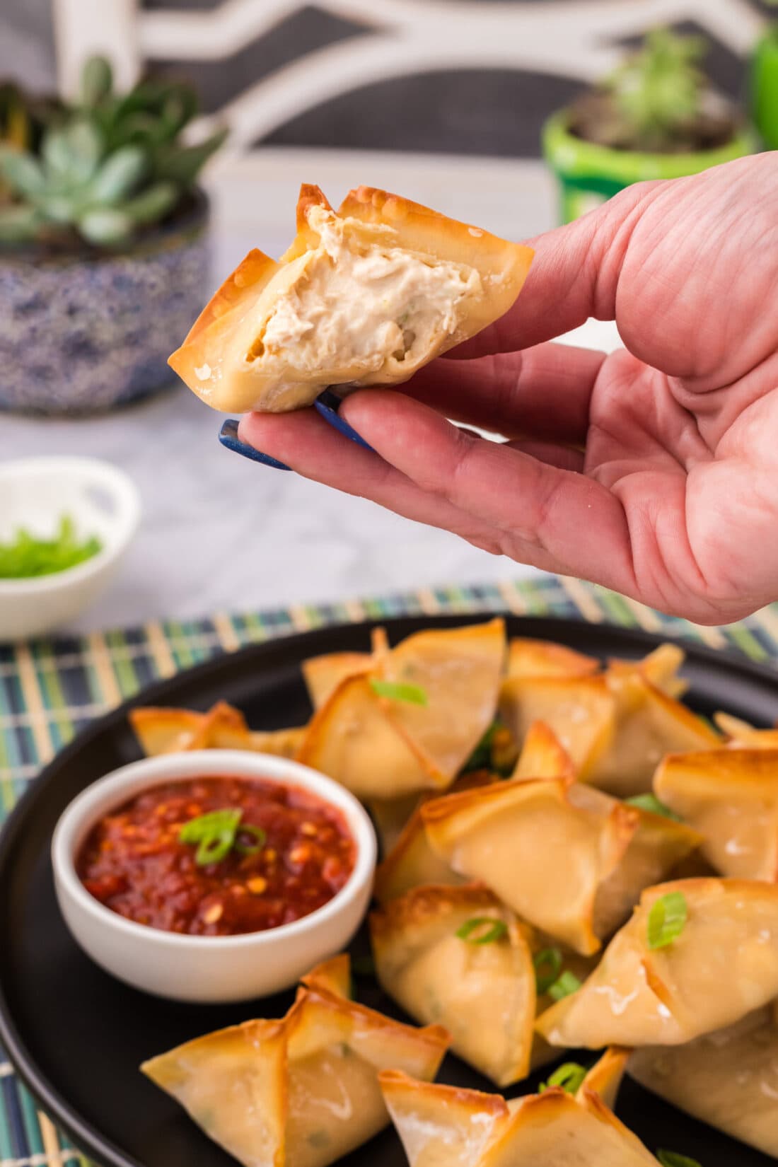 Hand holding up half of a Crab Rangoon showing the inside filling