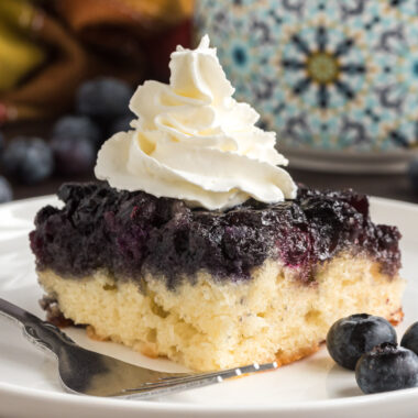 Square of Easy Blueberry Upside Down Cake on a plate topped with whipped cream